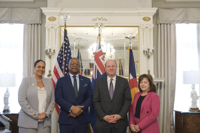 Four professionals standing in front of American, Turks and Caicos, and Colorado flags inside an elegant room with ornate decor and large windows.