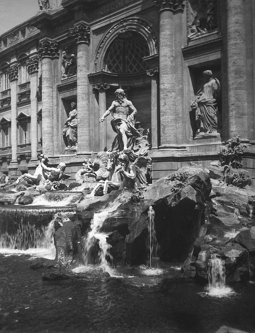 The image shows the Trevi Fountain in Rome, featuring ornate sculptures and flowing water. The backdrop includes large columns and intricate architectural details.