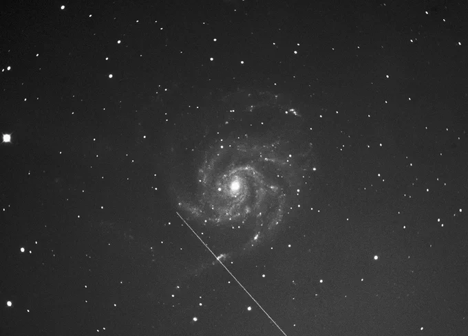 A Starlink satellite in Low Earth Orbit, against a background of the distant Pinwheel Galaxy. 