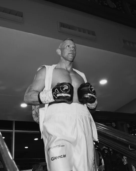 A focused male boxer in gloves and training attire prepares for a match. His determined expression underlines the intense mood of the scene.