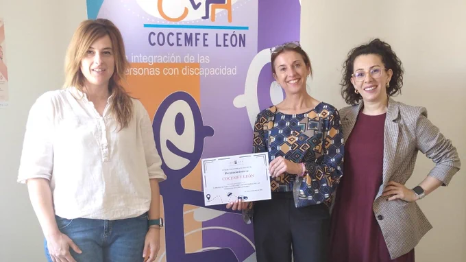 Foto de familia de los equipos técnicos de Integra CEE y Cocemfe León. Una de las profesionales de la entidad social, en el centro de la imagen, posa con un diploma de reconocimiento. Detrás de ellas, un roll up con la imagen corporativa de COCEMFE León y el mensaje "Por la integración de las personas con discapacidad".