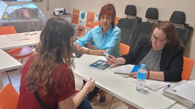 Momento de una entrevista presencial en las oficinas de Cocemfe Castelló. Dos técnicas del equipo de Integra CEE charlan con una usuaria de la entidad social. Las tres están sentadas de frente en una mesa rectangular de oficina con más mesas y sillas a su alrededor.