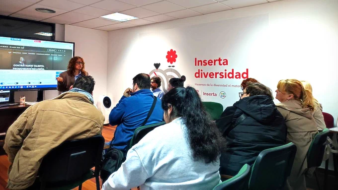 Espacio de formación con varias personas sentadas en sillas orientadas hacia una pantalla. Una persona expone junto a la pantalla en la que se visualiza la página web de Integra CEE. En la pared aparece el logotipo de Inserta Diversidad.
