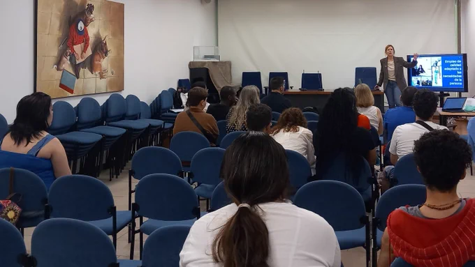Sala grande con varias filas de sillas ocupadas. En la parte frontal, una técnica de Selección de Integra CEE realiza una presentación mientras se muestra una diapositiva en una pantalla. El público está sentado mirando hacia ella.