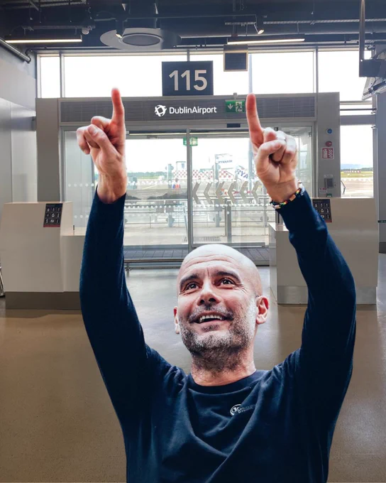 Picture of Pep Guardiola point upwards at Gate 115 in Terminal 1 at Dublin Airport, with the number 115 directly between his two fingers