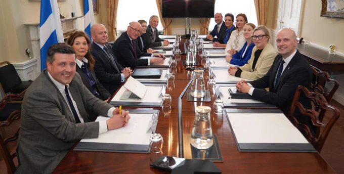 An image of the First Minister and the new cabinet sitting around a wooden table, they are smiling at the camera.