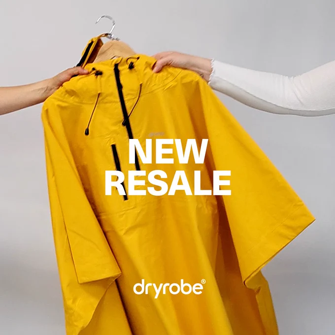 Two hands hold up a bright yellow Dryrobe waterproof poncho on a wooden hanger against a clean white background. The poncho features a black partial zipper and drawstring hood. Large white text overlays the centre reading "NEW RESALE", with the white Dryrobe logo featured at the bottom.