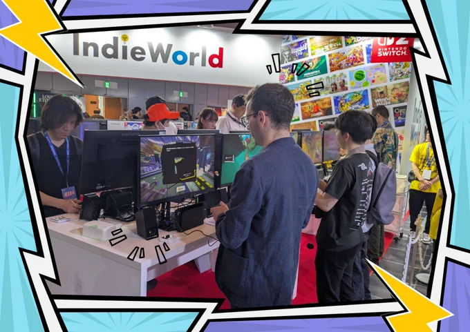 A row of standing tables with monitors and controllers with a backdrop title IndieWorld. People are playing the game denshattack at the booth.