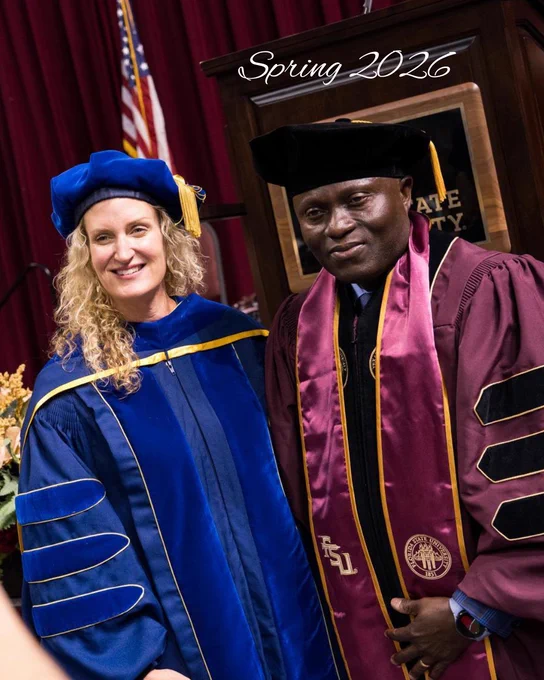 Two graduates in academic regalia posing indoors with a podium and American flag behind them, captioned Spring 2026.