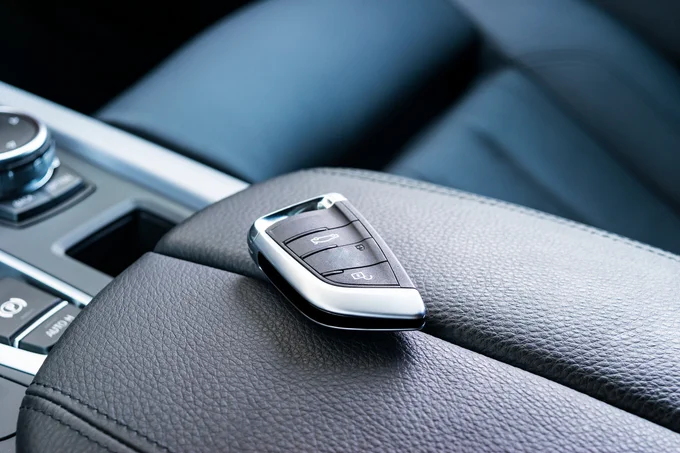 A modern car key with three buttons lies on the black leather armrest of a car's interior.