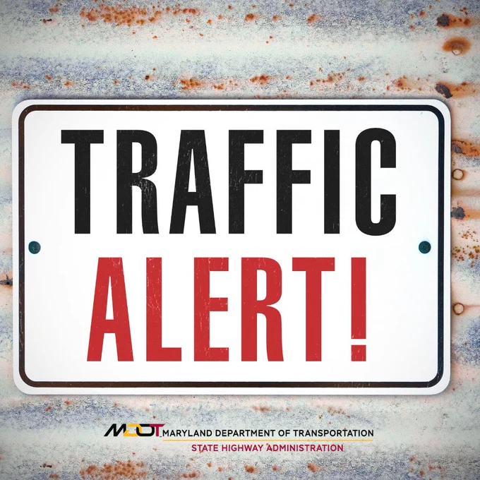 White rectangular sign with bold black text 'TRAFFIC' and red text 'ALERT!' mounted on a rusted metal surface.