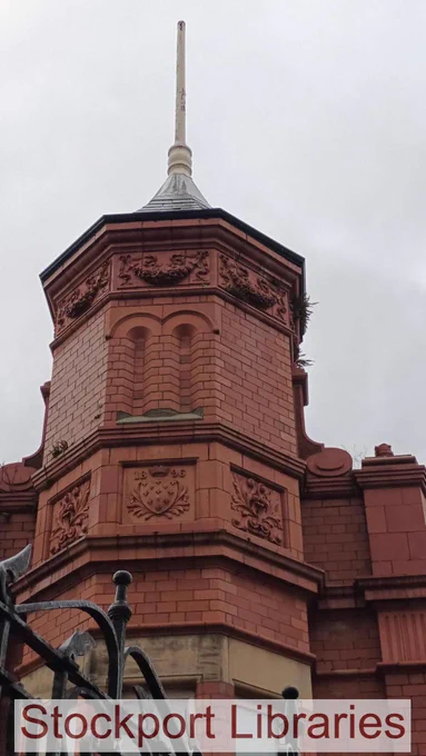 Ornate red brick tower with decorative carvings and a spire, under a cloudy sky.