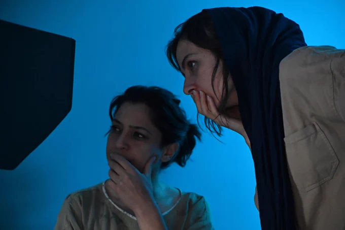 Two women with a blue background looking at camera footage behind the scenes.