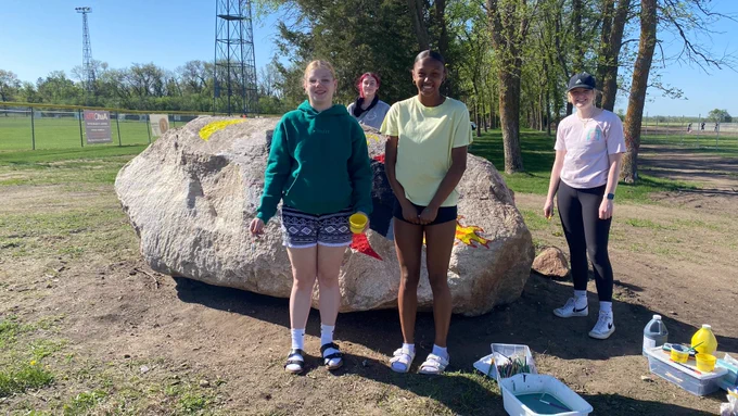 Students have supplies ready to start painting a mural on a big rock at the entrance to the field. 