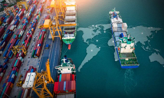 Aerial view of a busy container port with cranes loading cargo onto ships beside a digital world map overlay on the water.