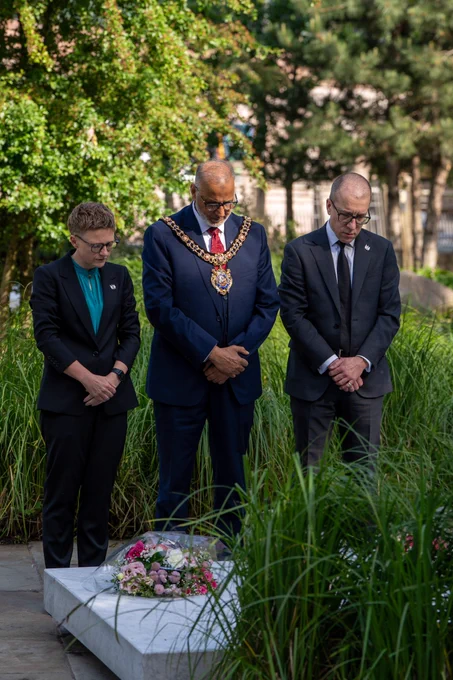 The Lord Mayor, the Leader of the Council, and the Chief Executive of Manchester Council stand with their hands crossed in the Glade of Light, in memory of the 22 that lost their lives in the Manchester Arena Bombing.