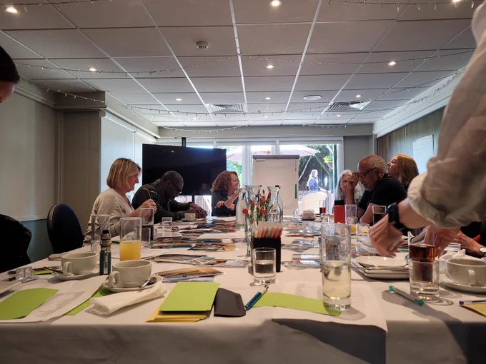 SILC staff gathered around a meeting table during an away day, with notes, photos, and refreshments spread out in a bright conference room.