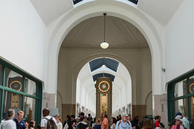 Crowded indoor hallway with arched ceilings and a large ornate clock at the far end under skylights.