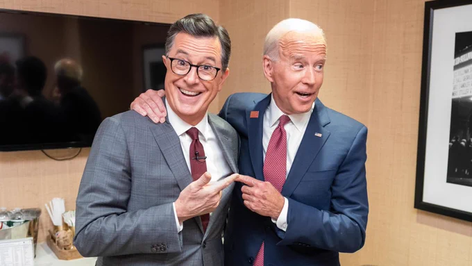 An image of Joe Biden and Stephen Colbert pointing at each other and smiling.
