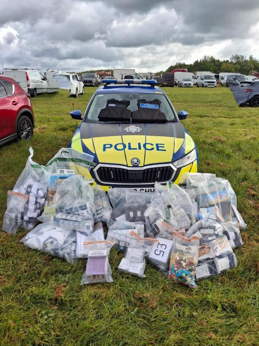 Police car with seized counterfeit goods including fake World Cup shirts and kits displayed on the grass in front.