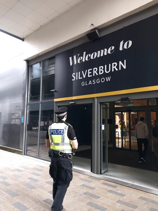 A police officer stands outside the entrance to Silverburn Glasgow, a shopping centre.
