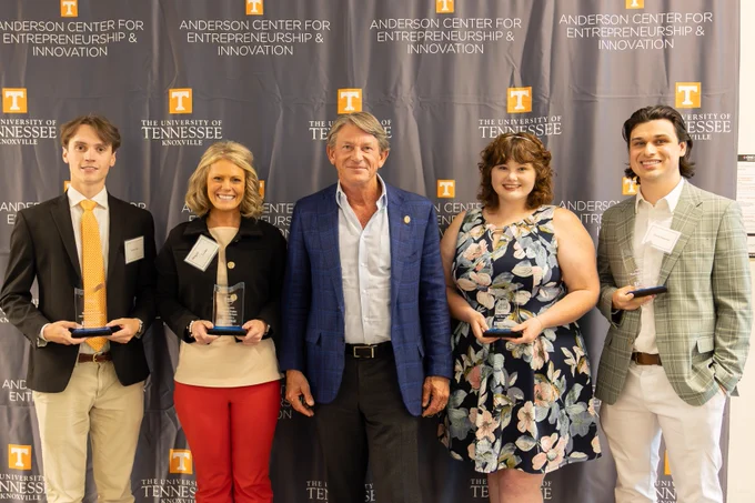 A group of five individuals stand in front of a backdrop that reads "Anderson Center for Entrepreneurship & Innovation" and "The University of Tennessee, Knoxville." Four of them hold awards. They are dressed in business and semi-formal attire.
