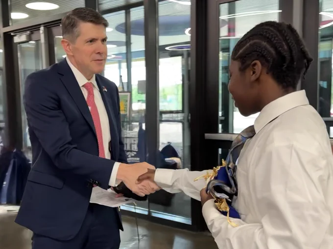 Treasurer Briner in a blue suit with red tie shaking a students hand