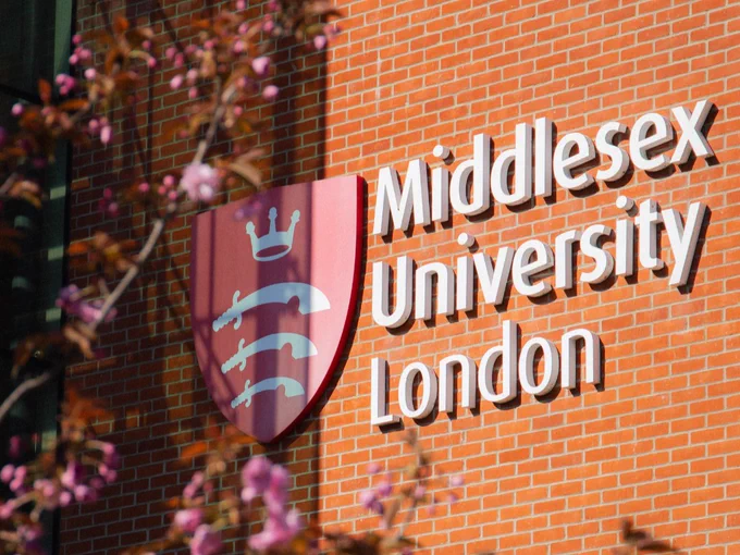 Brick wall featuring the Middlesex University London logo and name, partially obscured by blooming pink flowers in the foreground.