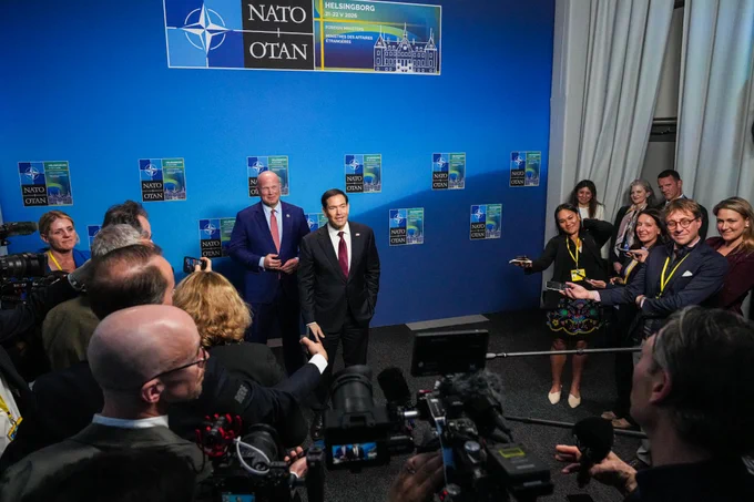 Secretary Rubio speaks with a group of journalists in Helsingborg, Sweden on May 22, 2026. He stands in front of a backdrop that has the NATO emblem in the middle. (State Department/Freddie Everett)