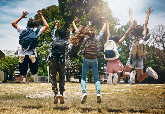 A group of chlidren enthusiastically jumping in the air, arms raised, in the playground at school.