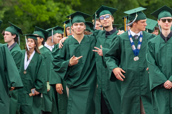 A group of graduates in green gowns enjoying their ceremony. They are smiling and posing for the camera, embodying a joyful and celebratory mood.