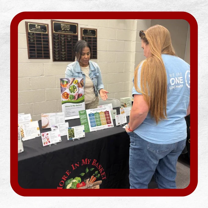 Woman at an informational booth with a "More In My Basket" display, talking to another person.