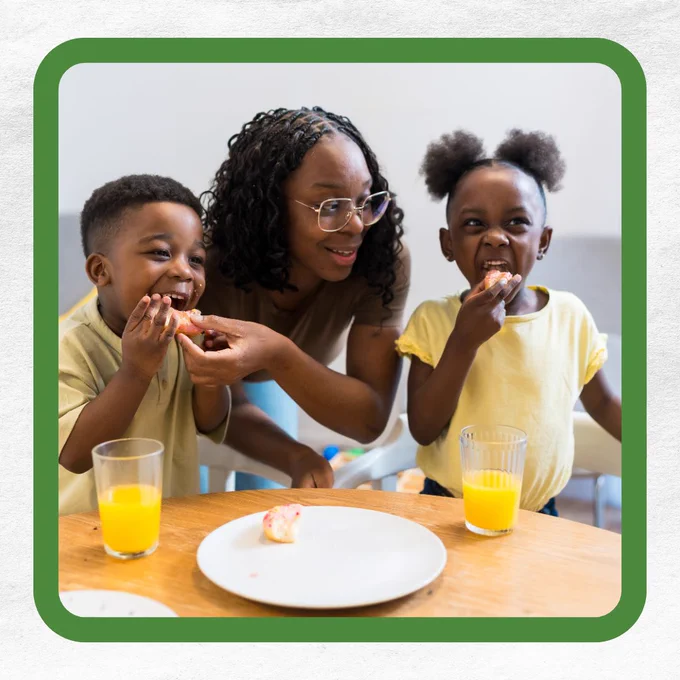 A woman and two young children enjoying fruit and orange juice at a table.