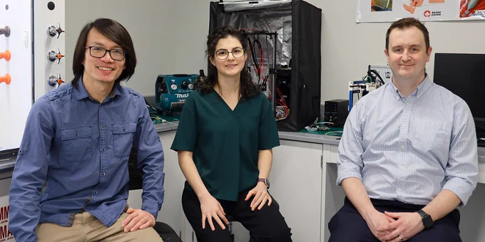 Harris (right) with assistant professor Eng Kuan Moo (left) and assistant professor Irina Garces (centre) sitting in a technology lab with various technical equipment and circuit boards on the counter behind them. 
