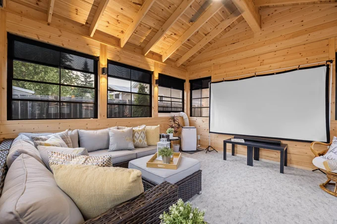 Cozy custom sunroom with wood interior, large windows, sectional seating, and a projector screen set up for movie nights.