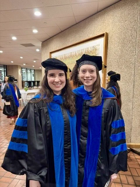 Two graduates smiling in academic regalia