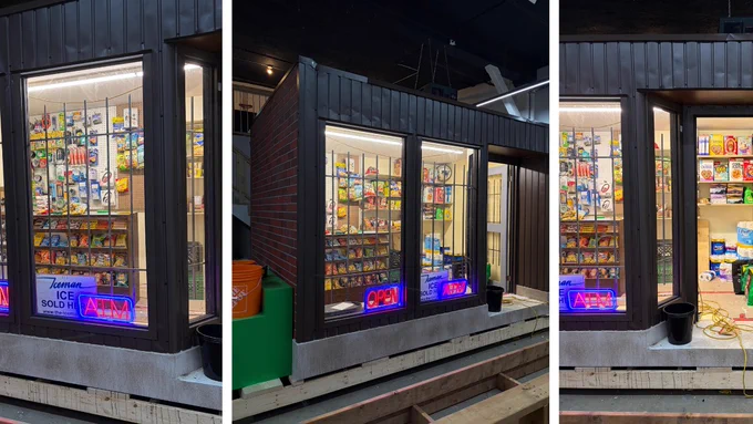 Sneak peak into the artwork that looks like a convenience store with a dark exterior and large glass windows displaying various snacks and goods. Bright neon signs in the windows say "Open" and "ICE SOLD HERE." The interior is brightly lit and shelves are stocked with colorful packaging.