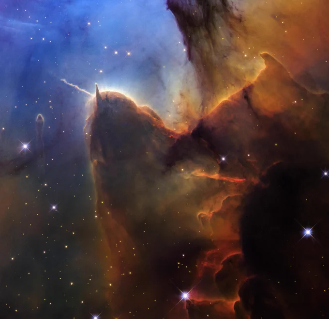 Vista de Hubble con un encuadre muy cerrado de una vasta región de formación estelar conocida como la nebulosa Trífida. La parte superior izquierda es de color azul brillante. Colores en marrón y ámbar se extienden desde la parte superior derecha, atravesando el centro de la imagen en líneas irregulares y superpuestas, hasta llegar a la zona central inferior. En la parte inferior derecha, la imagen es casi negra. Pequeñas estrellas de color ámbar se ven en toda la escena. Hacia la izquierda, hay una prominente forma marrón que recuerda una cabeza con dos cuernos. El cuerno izquierdo apunta hacia la izquierda y tiene forma ondulada. El cuerno derecho es triangular y apunta hacia arriba. 