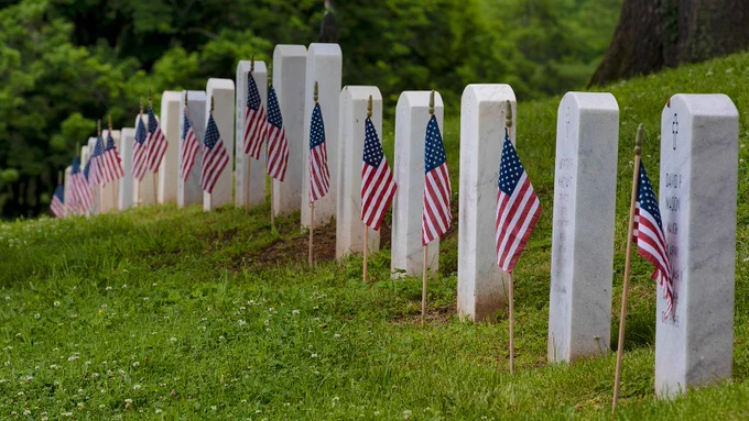 Eight white headstones in a row, each with an American flag.