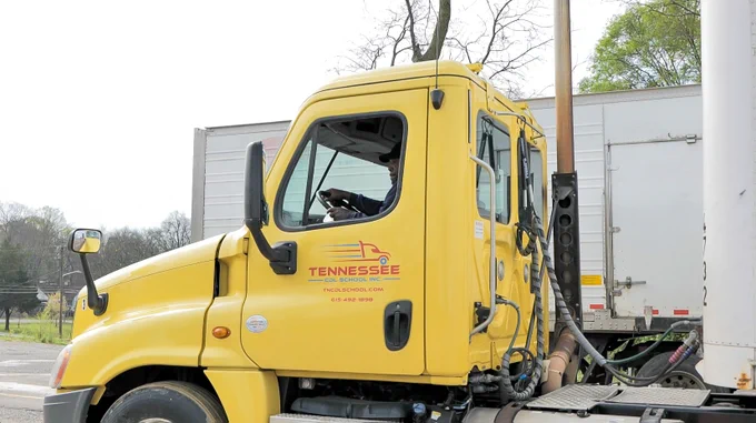 Yellow semi-truck cab parked beside a white trailer on a clear day.