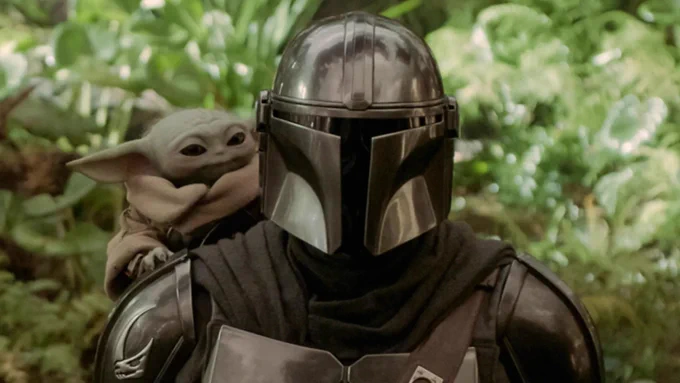 Grogu on the shoulder of the Mandalorian in a jungle. 