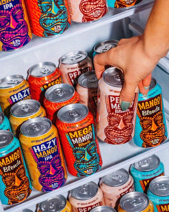A vibrant display of craft beer cans in a refrigerator, with a hand selecting a peach mango-flavored can. The scene exudes a fun and colorful vibe.