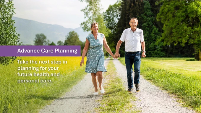 A husband and wife walk down a scenic gravel path surrounded by leafy green trees and tall grass. They are holding hands and smiling. Text on the image reads: “Advance Care Planning” and “Take the next step in planning for your future health and personal care.”