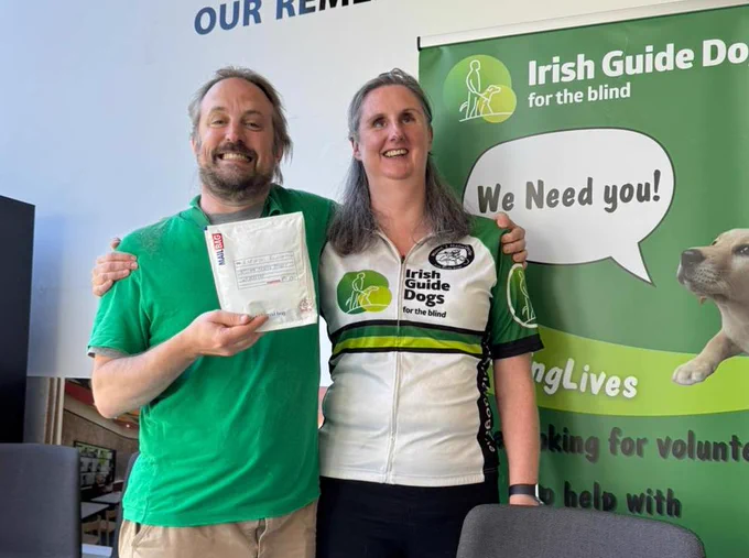 Geraldine and myself with our arms around each others' shoulders, smiling to the camera. I am holding the envelope with my hair in it ready to send. What is left of my hair is a bit messy! The poster to Geraldine's left has a puppy with a speech bubble saying "we need you!"