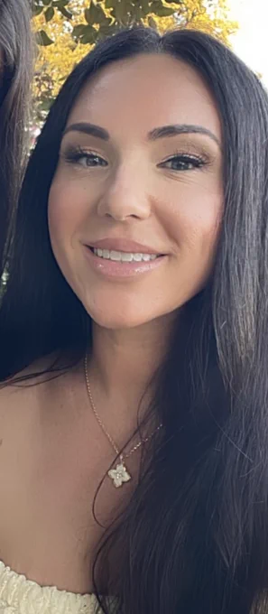 Smiling woman with long dark hair against a background of autumn leaves.