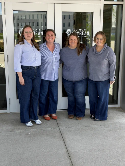 Four women stand in front of a building smiling. 