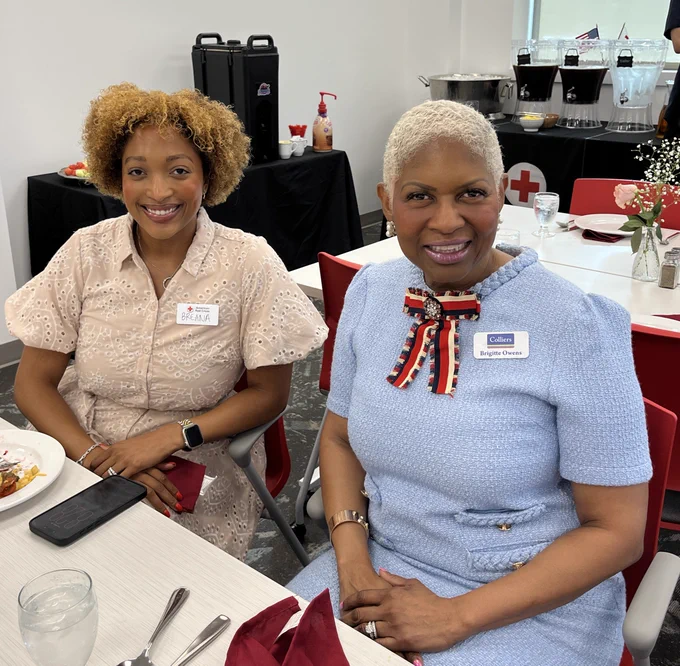 Two people in business casual attire smile at the camera. They are seated at a table.