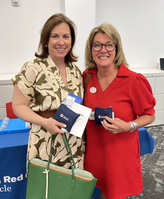 Two Red Crossers hold small, eco-friendly blue bags folded into squares and smile at the camera.