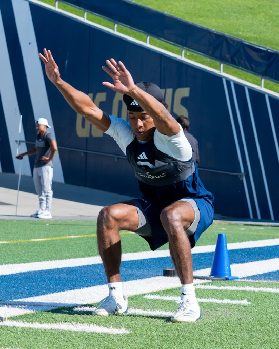 UC Davis student athlete lands on broad jump and keeps balance while on the football field while wearing a blue shirt and blue pants with white cleats