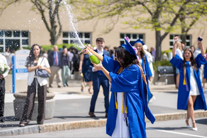 A graduate sprays a bottle of champagne in front of the center for the arts.